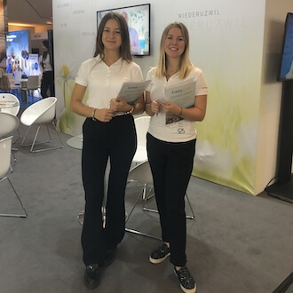 Zwei Interviewerinnen auf einer Messe, lächelnd mit Umfragebögen in der Hand