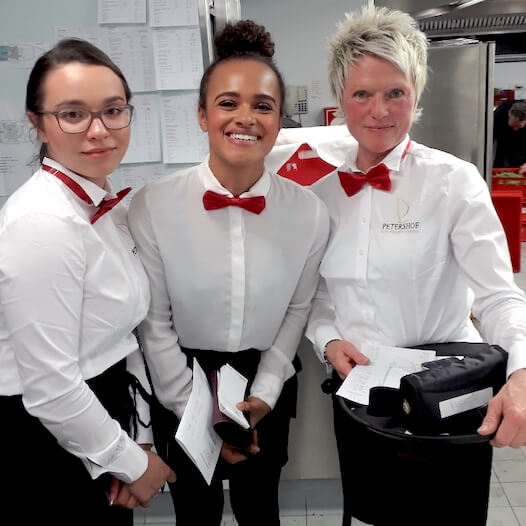 Drei Servicekräfte in einheitlicher Uniform mit Fliege und Notizblock im Einsatz für einen À-la-carte-Service in einem Restaurant oder Eventbetrieb